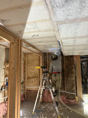 Installer blowing insulation into netting across an open basement ceiling