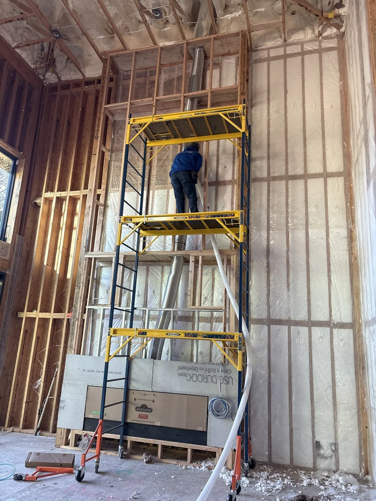 Interwest installer working from a three-tier scaffold on a tall blown-in insulation wall