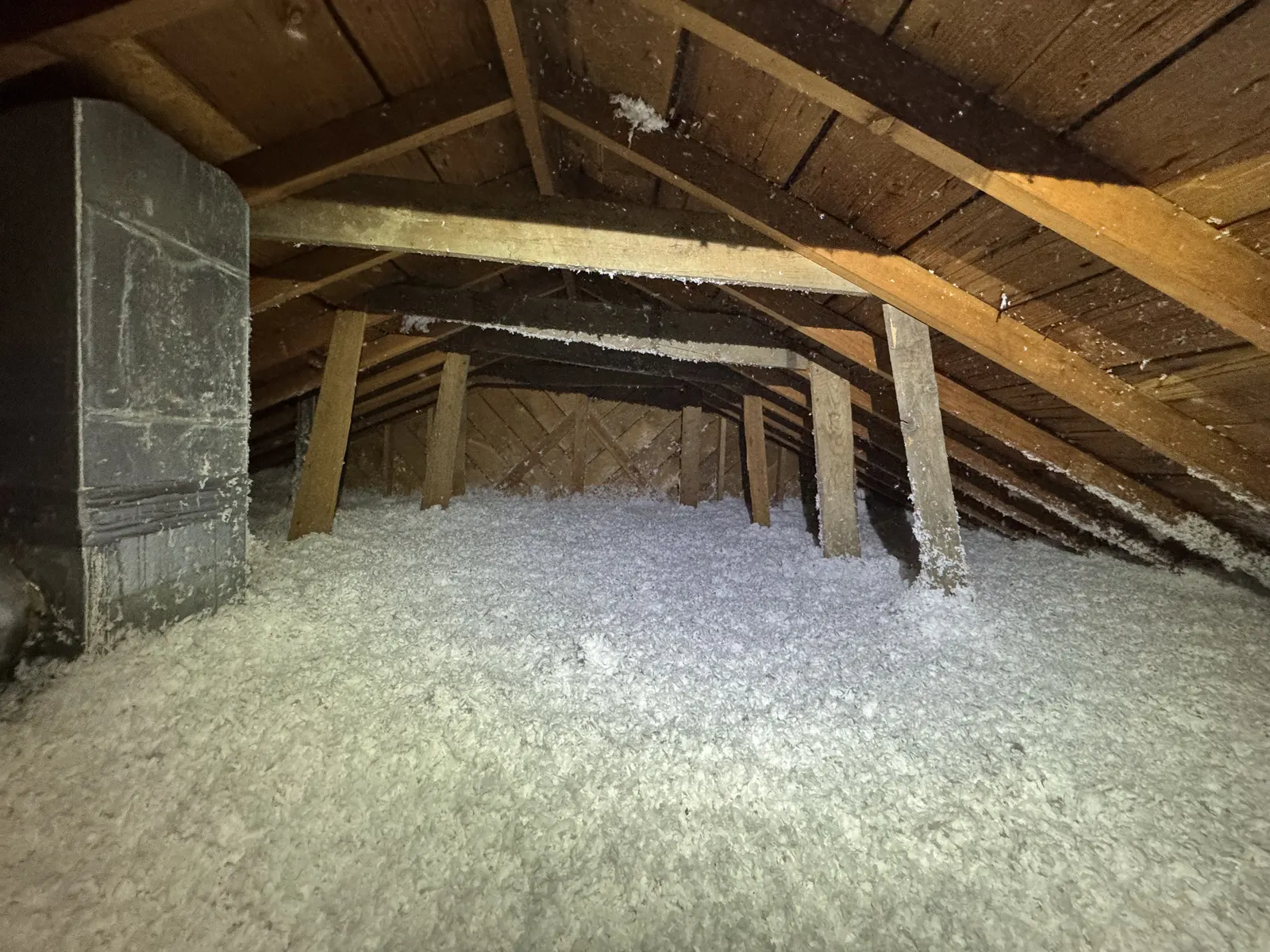 Loose-fill insulation covering an older attic floor around framing and a masonry flue