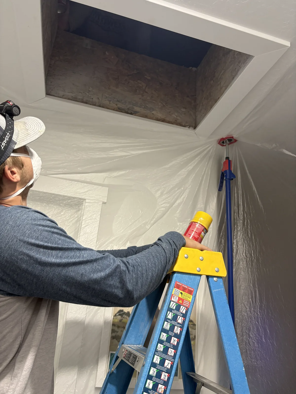 Interwest installer working from a ladder inside a plastic-protected living room