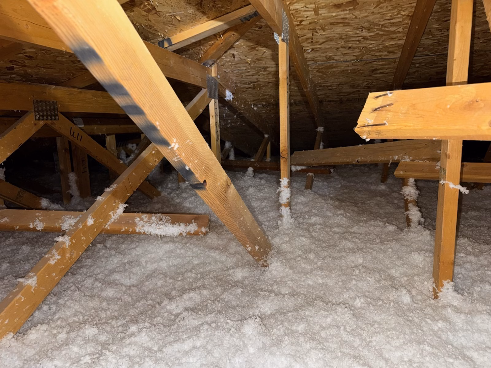 Fiberglass loose-fill insulation covering the attic floor beneath roof trusses in Draper, Utah.